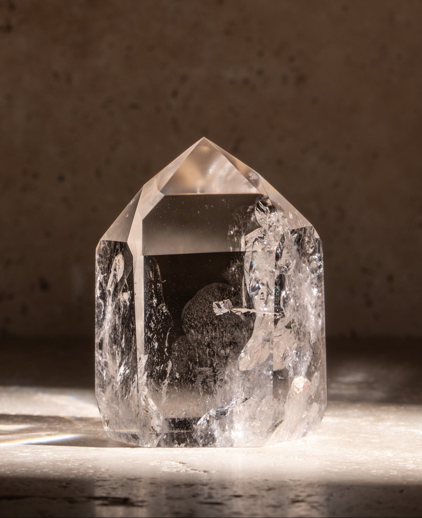 A polished AAA quality Clear Quartz tower with a sharp, faceted tip and clear, smooth surface reflecting natural light.