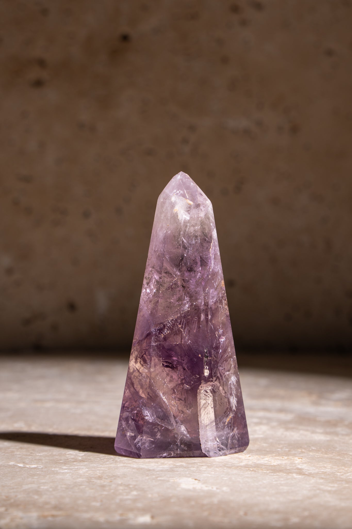 A polished Amethyst crystal point featuring a rich purple color with intricate internal patterns, showcasing natural inclusions.