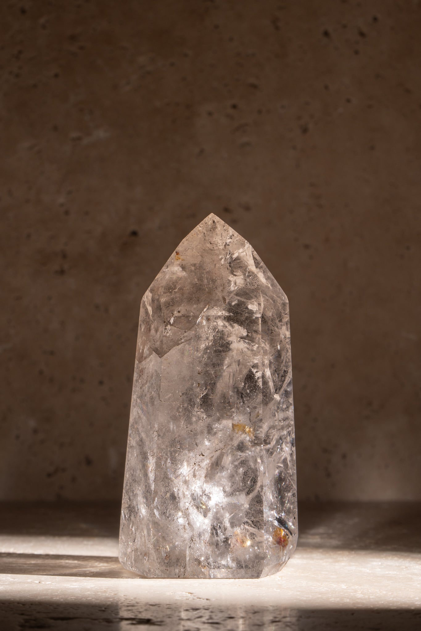 A polished AAA quality Clear Quartz tower with a sharp, faceted tip, clear surfaces, and natural inclusions, catching light beautifully.