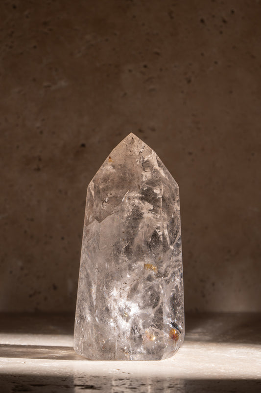 A polished AAA quality Clear Quartz tower with a sharp, faceted tip, clear surfaces, and natural inclusions, catching light beautifully.