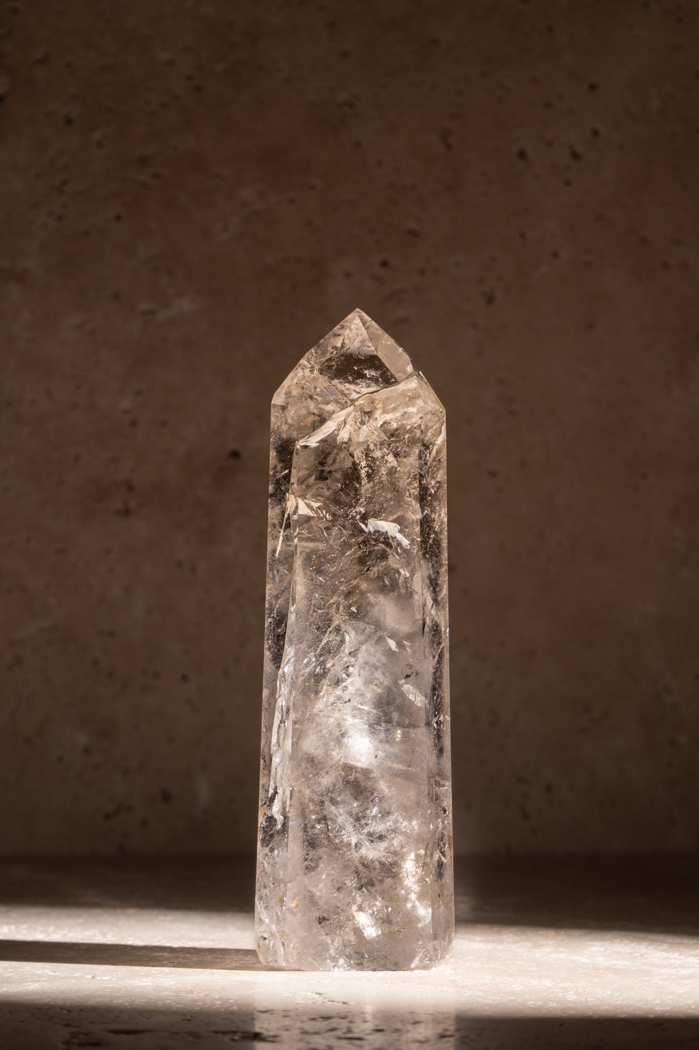 A polished AAA quality Clear Quartz tower with a sharp, faceted tip, clear surfaces, and natural inclusions, catching light beautifully.