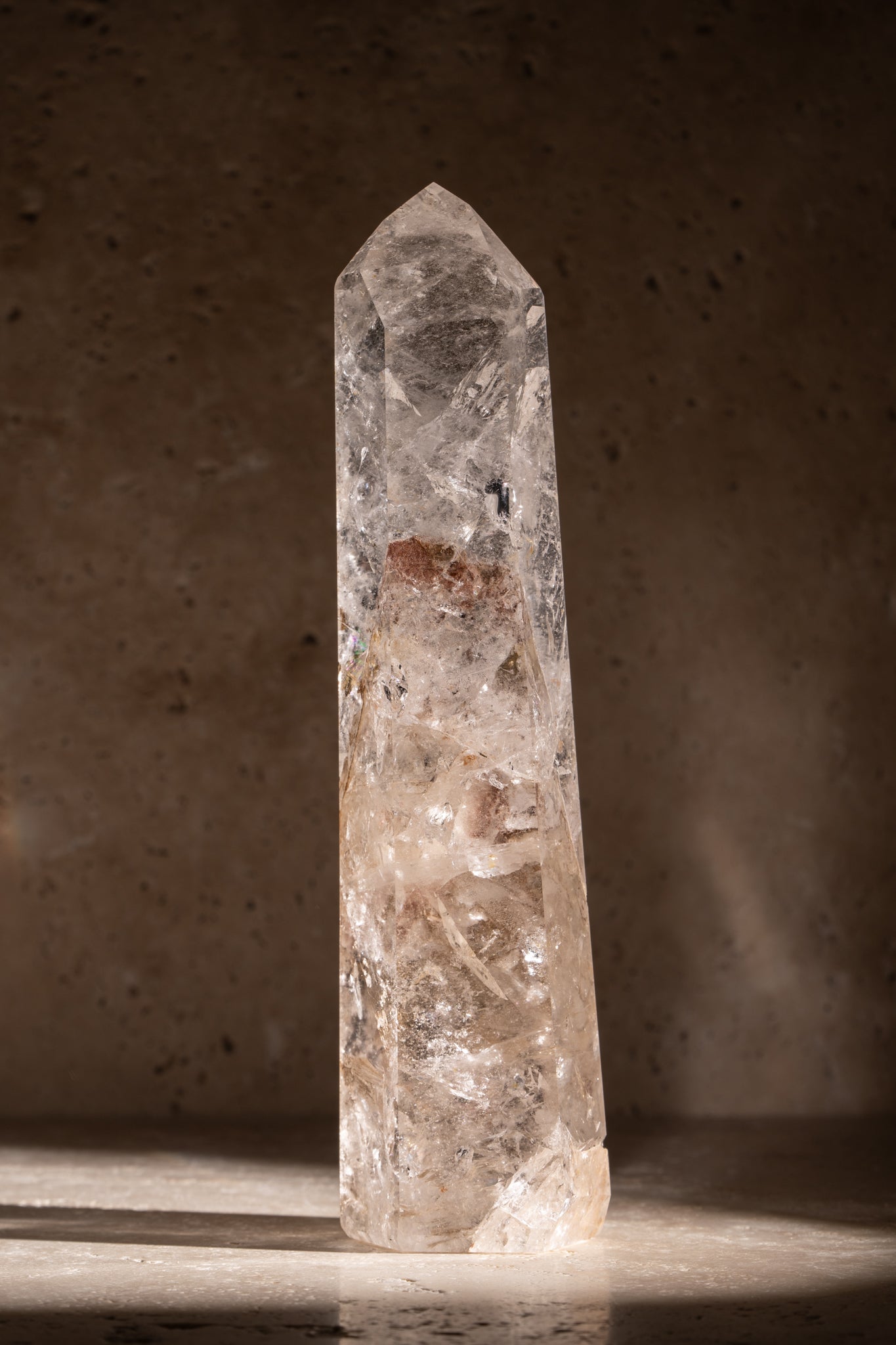 A polished AAA quality Clear Quartz tower with a sharp, faceted tip, clear surfaces, and natural inclusions, catching light beautifully.