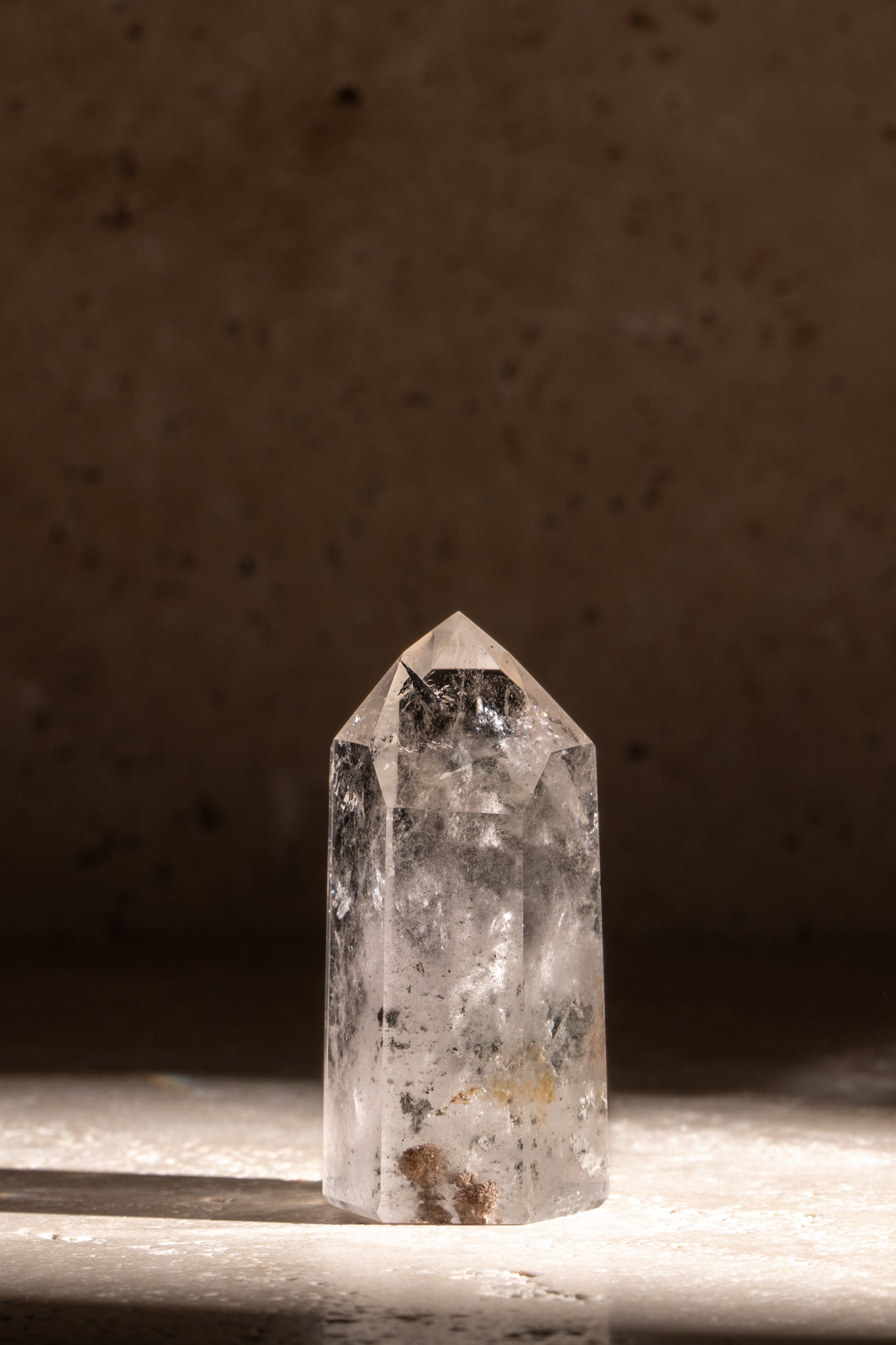 A polished AAA quality Clear Quartz tower featuring a sharp, faceted tip, with natural inclusions showcasing its clarity and energy.