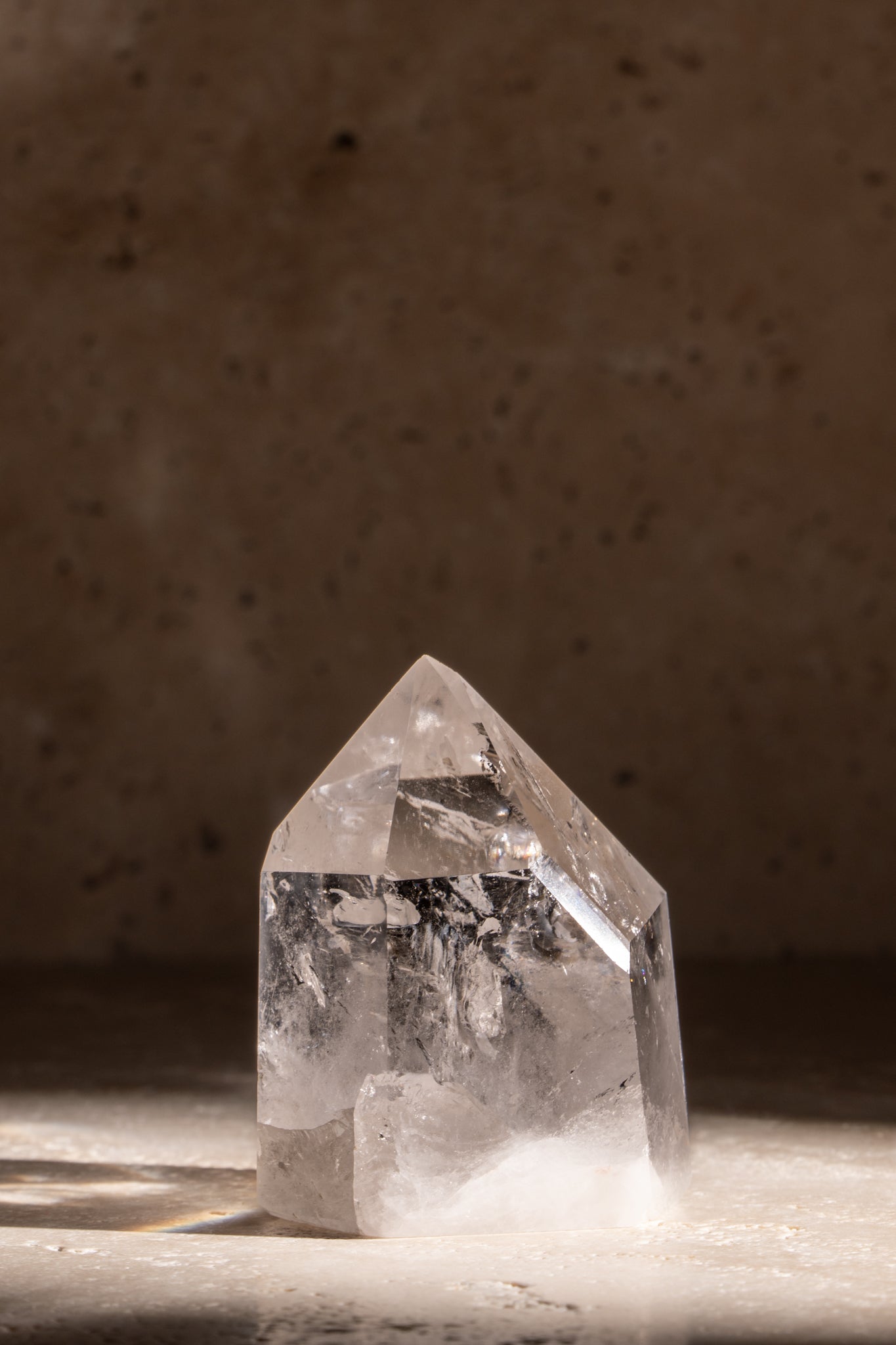 A polished AAA quality Clear Quartz tower featuring a sharp, faceted tip, highlighting the clarity and natural inclusions within the crystal.