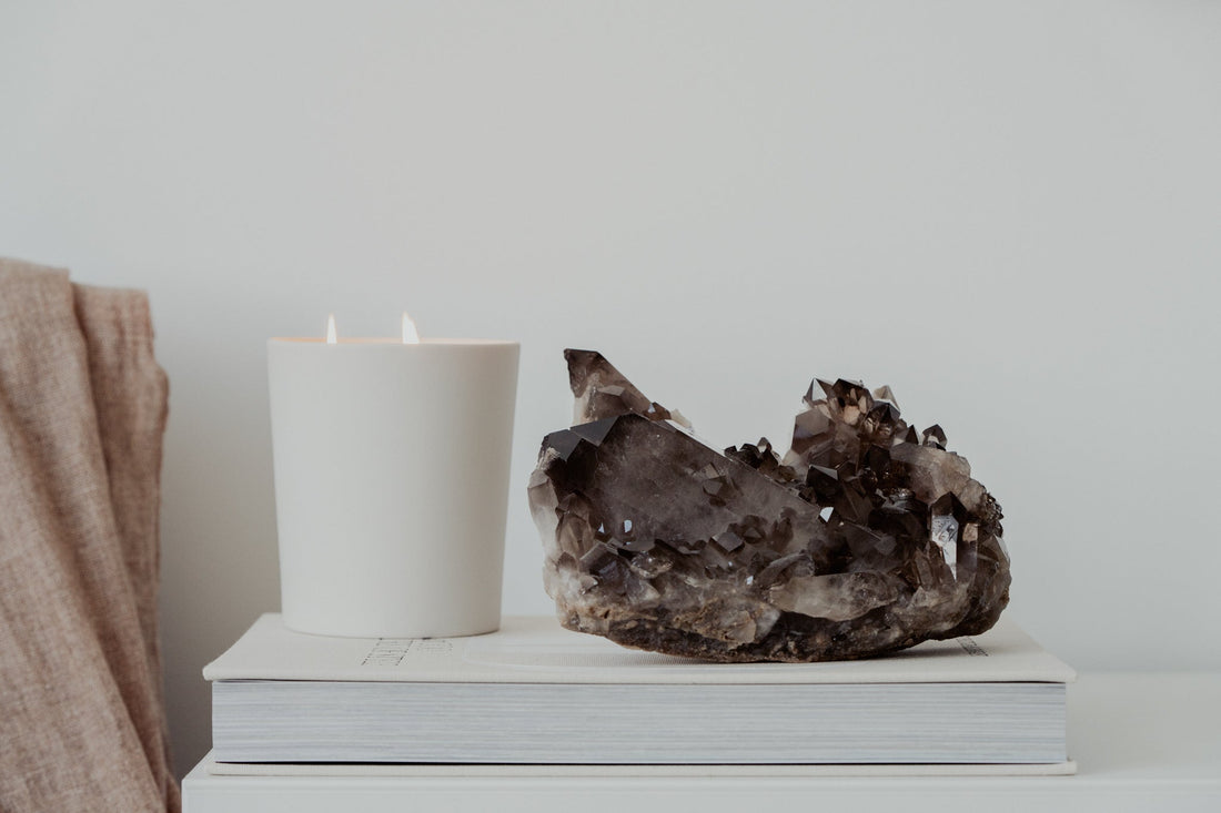 Smoky quartz cluster on a book with soft fabric and a lit candle, styled for a calm and grounding home atmosphere.