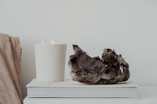 Smoky quartz cluster on a book with soft fabric and a lit candle, styled for a calm and grounding home atmosphere.