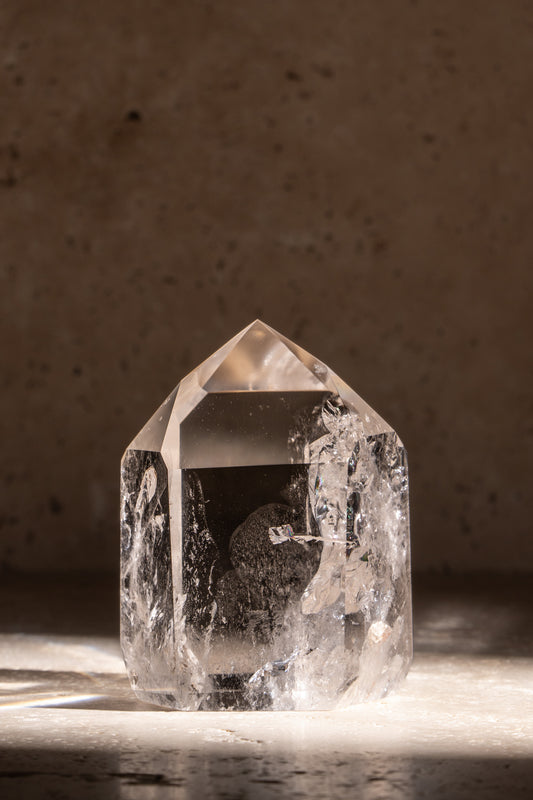 A polished AAA quality Clear Quartz tower with a sharp, faceted tip and clear, smooth surface reflecting natural light.