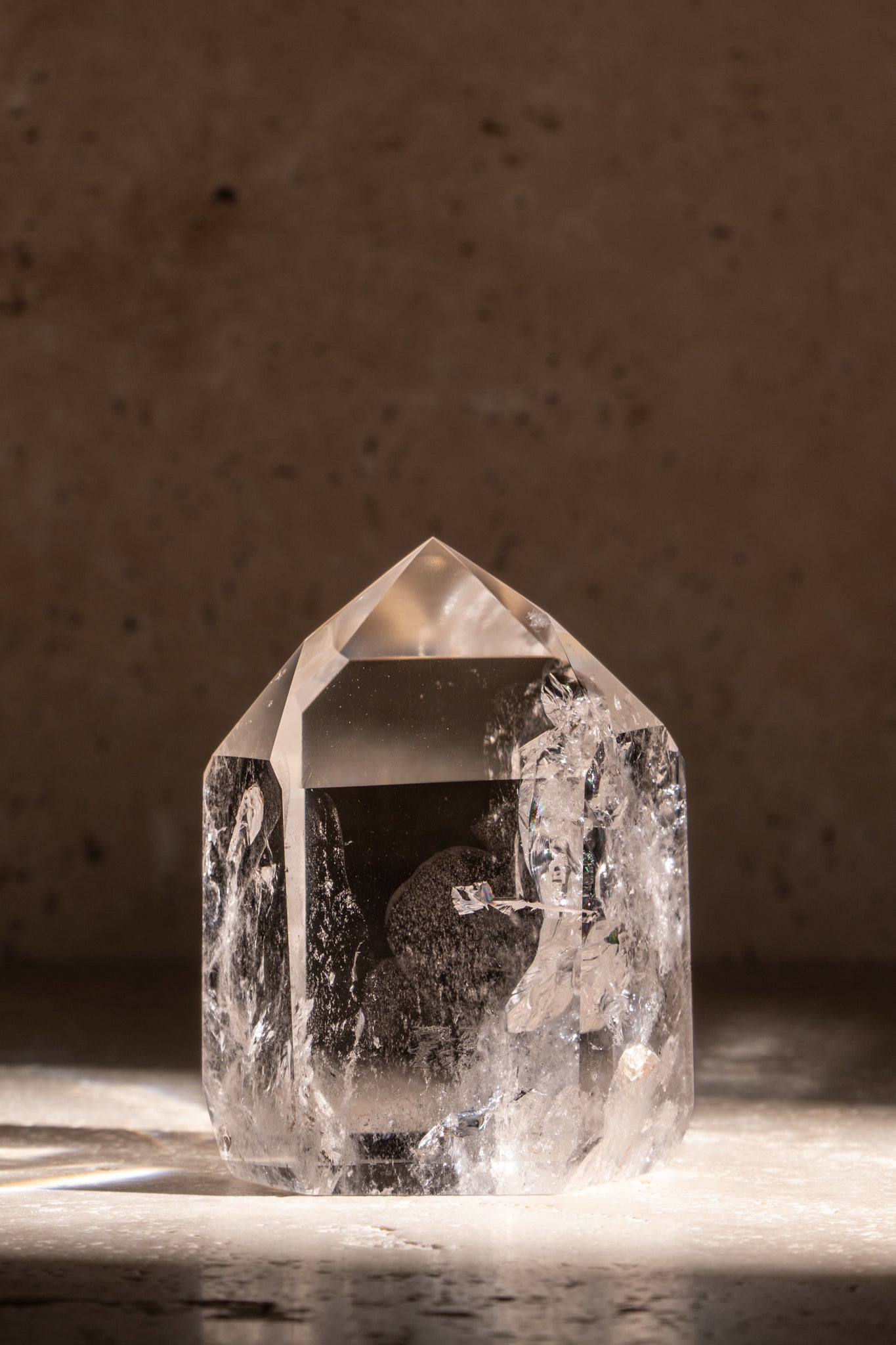 A polished AAA quality Clear Quartz tower with a sharp, faceted tip and clear, smooth surface reflecting natural light.