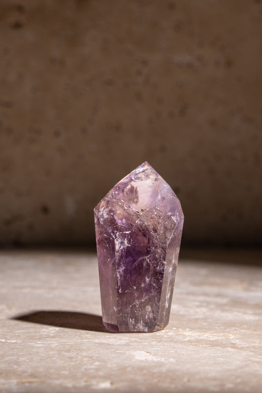 A polished Amethyst crystal tower with deep purple hues and visible natural inclusions, adding a calming and healing energy.