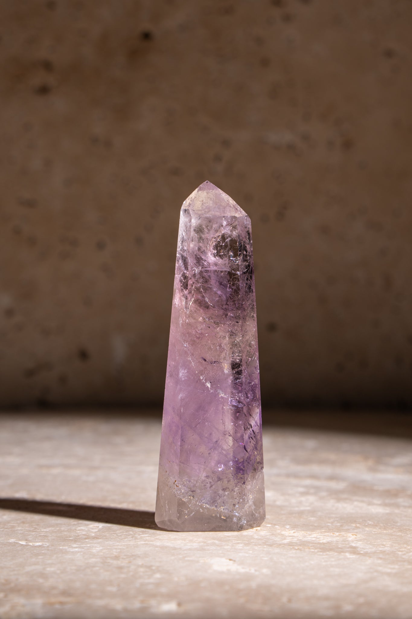 A polished Amethyst crystal tower with rich purple tones, showcasing intricate internal inclusions and a faceted tip.