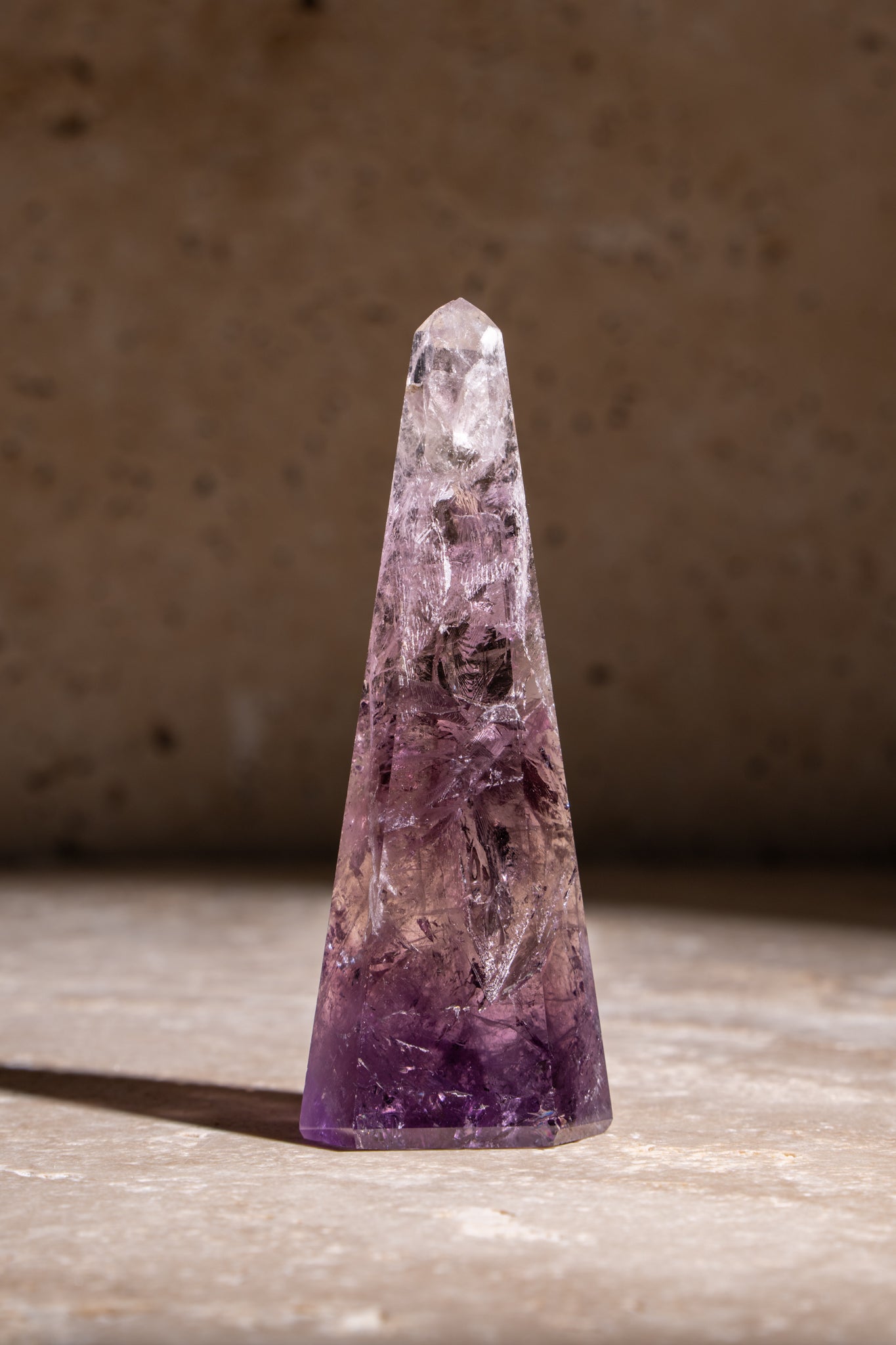 A polished Amethyst crystal tower with rich purple hues and intricate internal inclusions, showcasing a faceted tip.