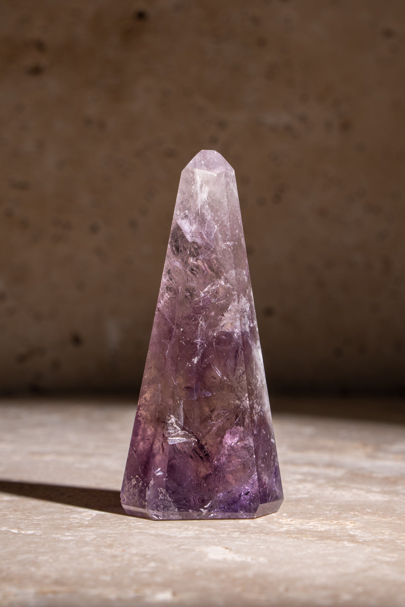 A polished Amethyst crystal tower with intricate internal inclusions and a rich purple hue, finished with a faceted tip.