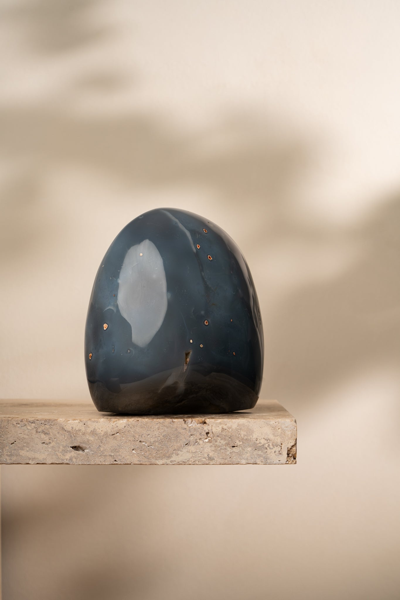 A polished Blue Agate freeform with deep blue and gray hues, featuring smooth curves and small natural inclusions that create a unique, soft pattern.