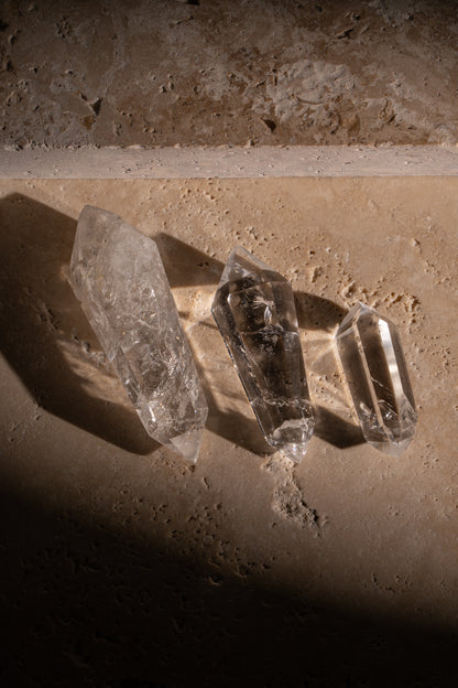 A set of three polished AAA quality Clear Quartz Double Terminated crystals with sharp, faceted tips on both ends, showcasing their exceptional clarity and natural inclusions.