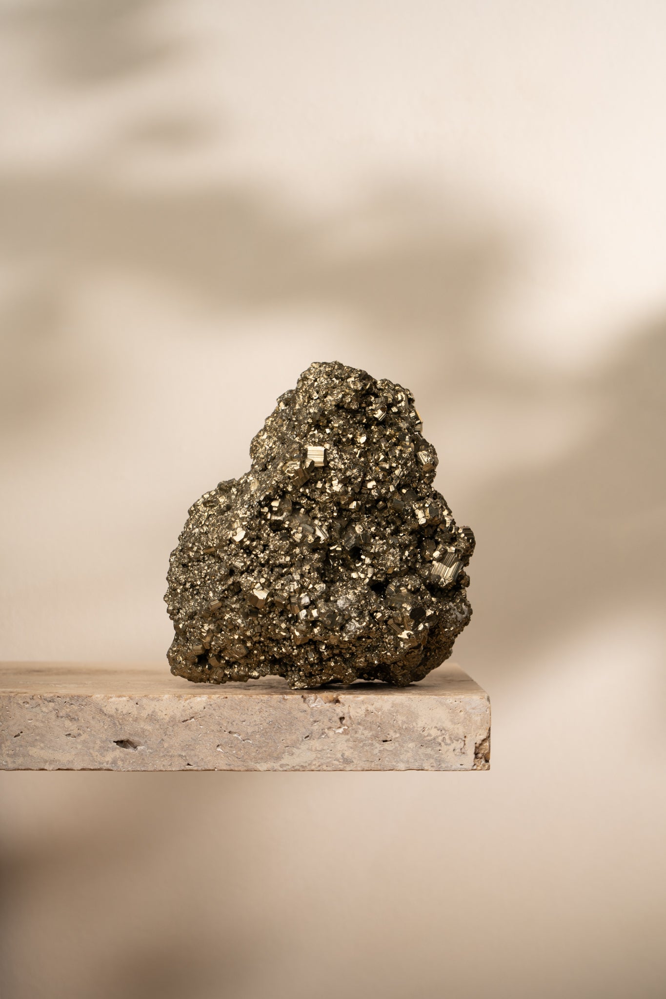 A raw Pyrite cluster with small cubic formations and a metallic gold sheen, sitting on a neutral stone surface with soft lighting.